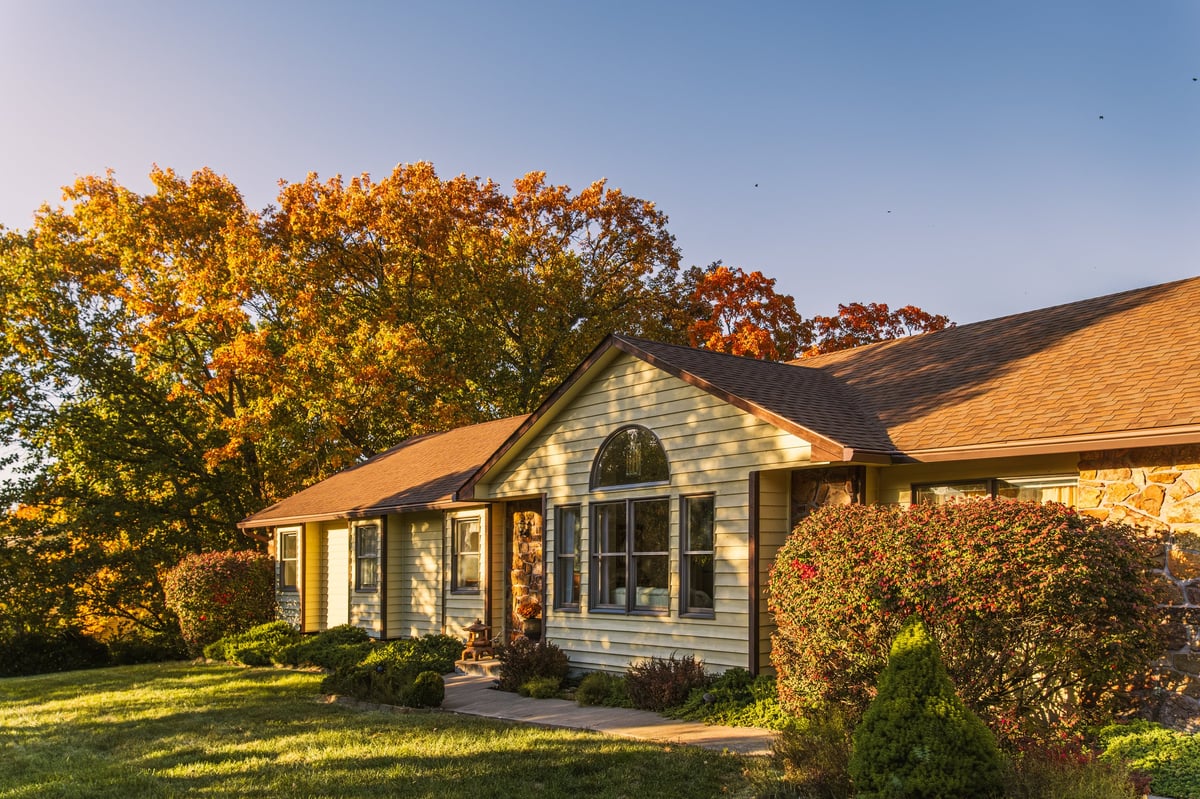 Midwestern suburban house in fall at sunset; large trees with autumn foliage behind house and long shadows on the lawn.