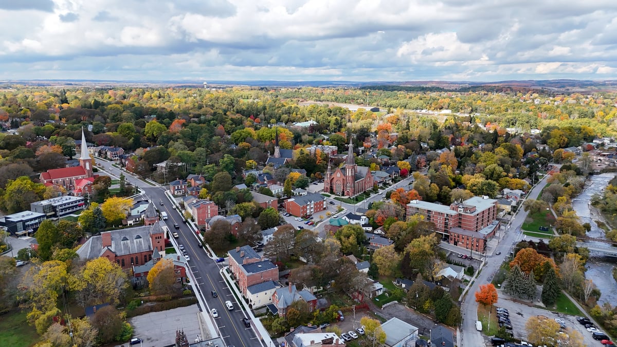 The aerial view showcases a mix of residential and commercial properties and historic buildings, surrounded by lush trees displaying a kaleidoscope of fall colors
