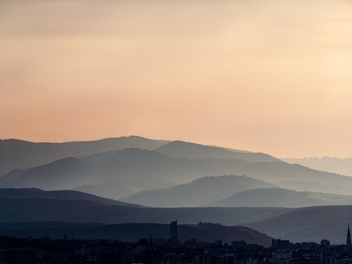 Evening atmosphere above layered mountain silhouettes and distant city skyline at sunset.